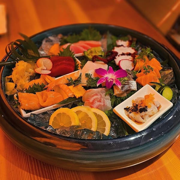 A large platter of colorful sashimi and seafood, garnished with lemon, radish, and an orchid.