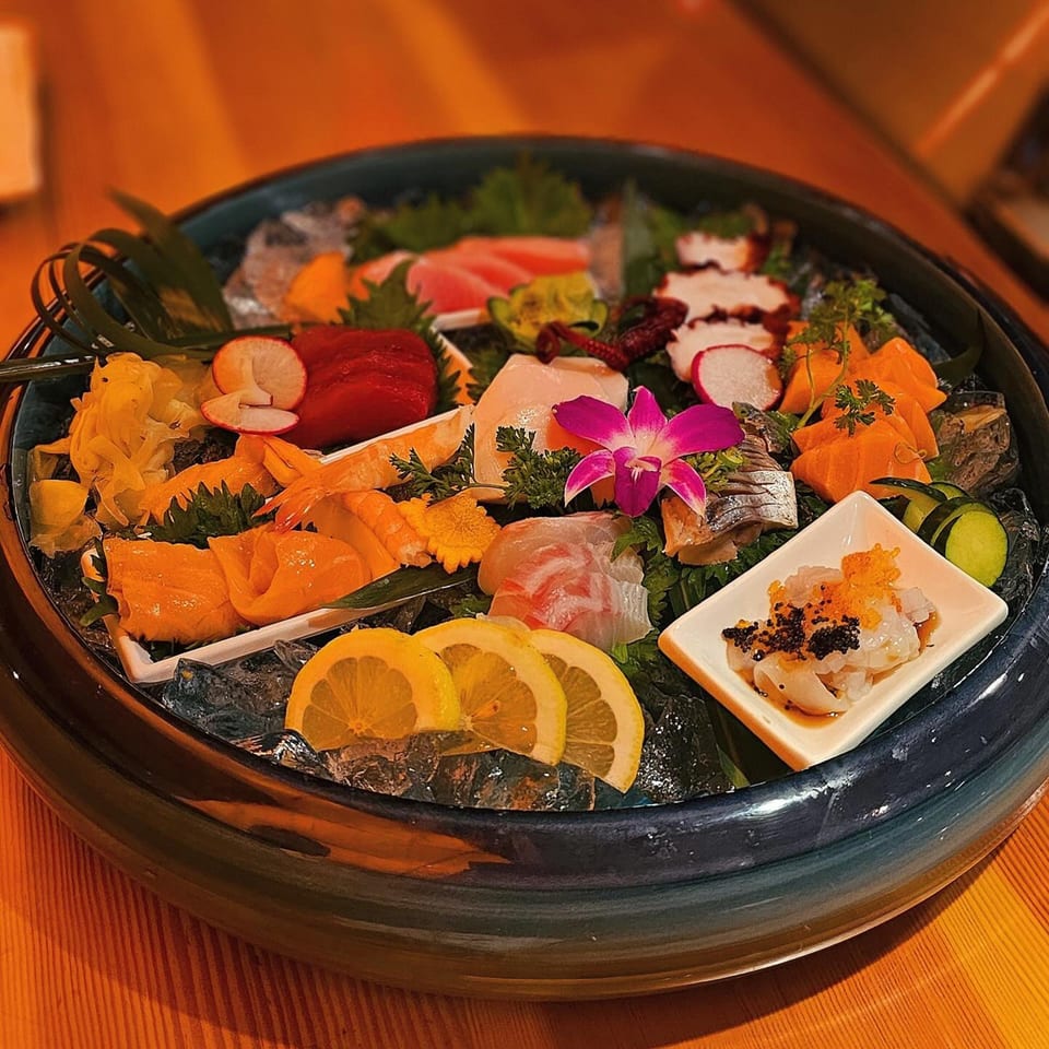 A large platter of colorful sashimi and seafood, garnished with lemon, radish, and an orchid.