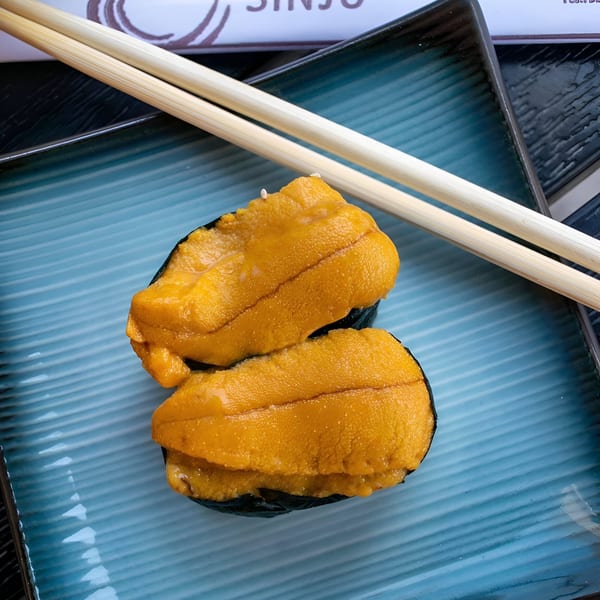Two pieces of uni sushi with bright orange sea urchin on a blue plate with chopsticks.
