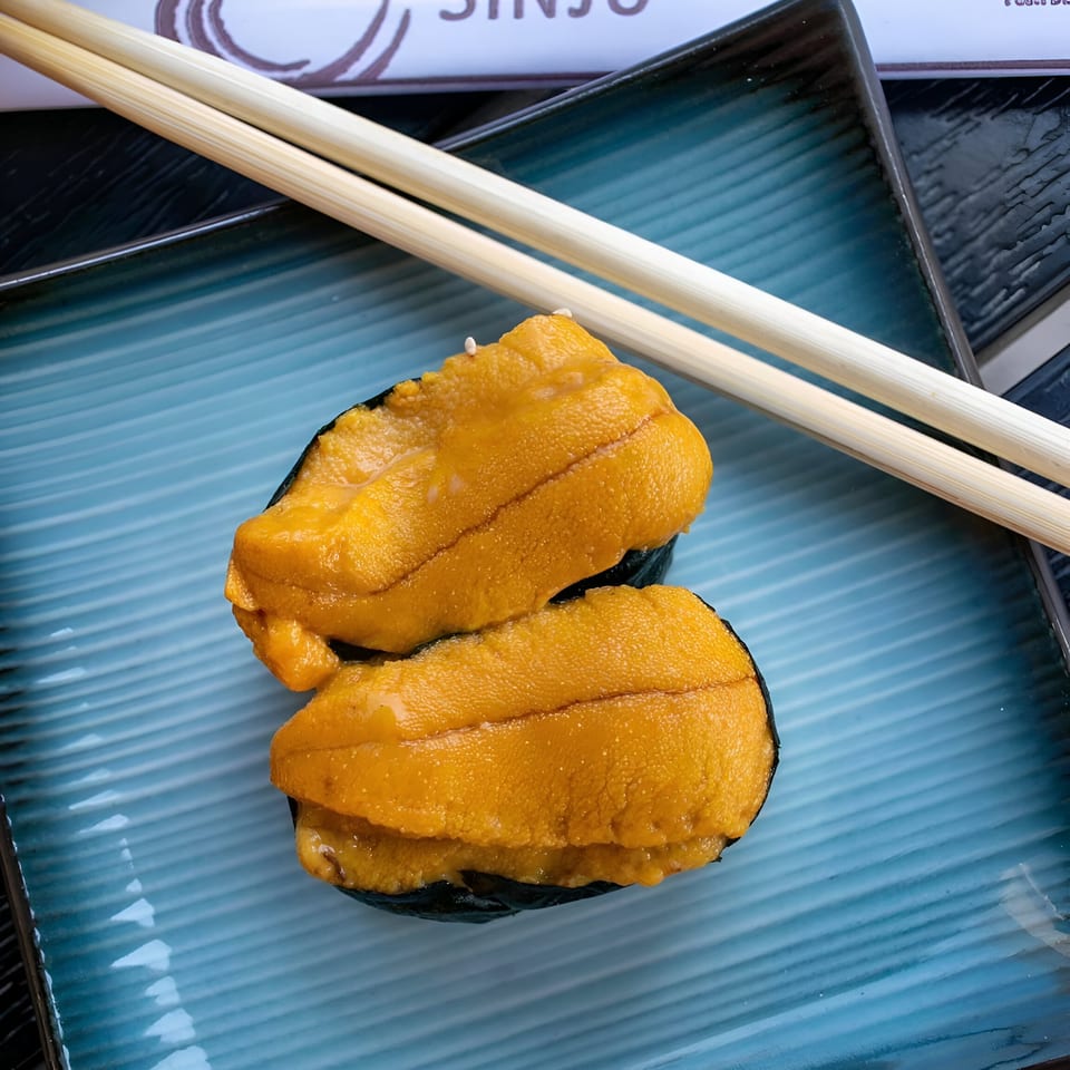 Two pieces of uni sushi with bright orange sea urchin on a blue plate with chopsticks.