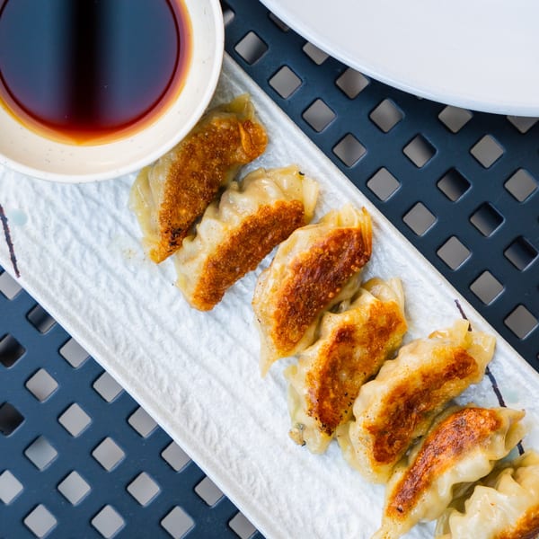 A white rectangular plate of golden-brown gyoza dumplings with a side of soy sauce.