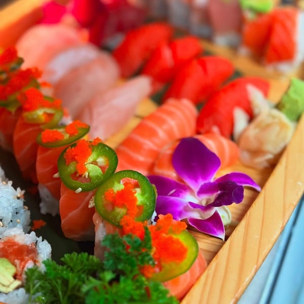 A wooden platter filled with various Sinju Sushi rolls, sashimi, and nigiri, garnished with a purple orchid.