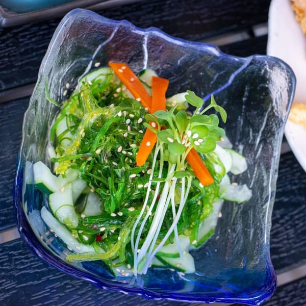Sinju Sushi's seaweed salad with cucumbers, carrots, and sesame seeds in a blue glass bowl.