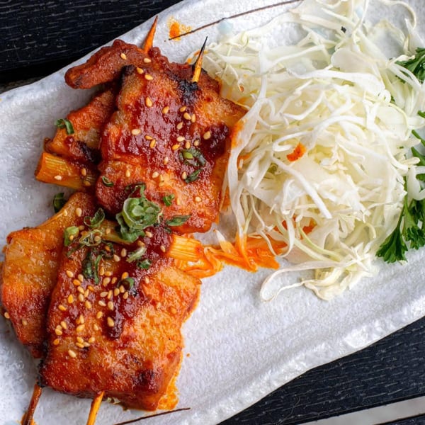 Grilled Japanese skewers with red sauce, sesame seeds, and green onions, served with shredded cabbage.