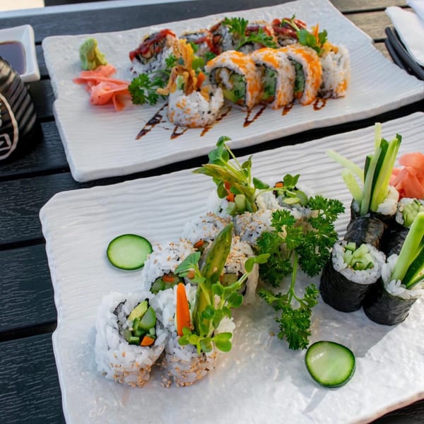Two plates of colorful Sinju Sushi rolls, garnished with fresh herbs and served with ginger and wasabi.