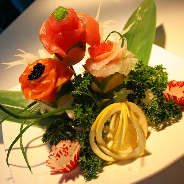 Artfully arranged Sinju Sushi sashimi roses with caviar, parsley, lemon, and radish on a white plate.