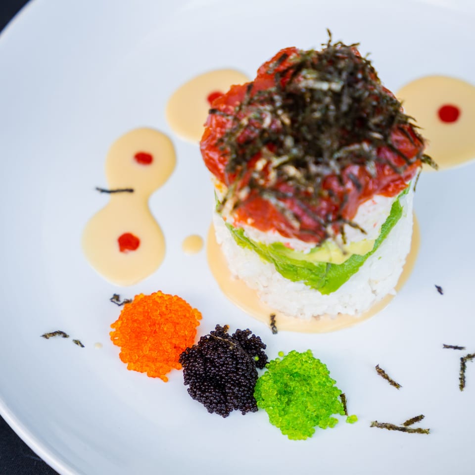 Sinju Sushi's colorful tuna tower with avocado, rice, and three types of tobiko on a white plate.