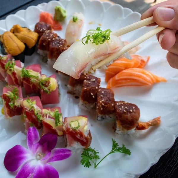 Chopsticks picking up a piece of sushi from a platter of various Sinju Sushi rolls and nigiri.